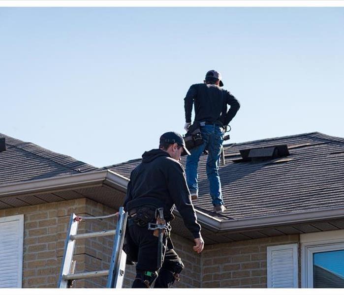Two roofers inspecting a damaged roof